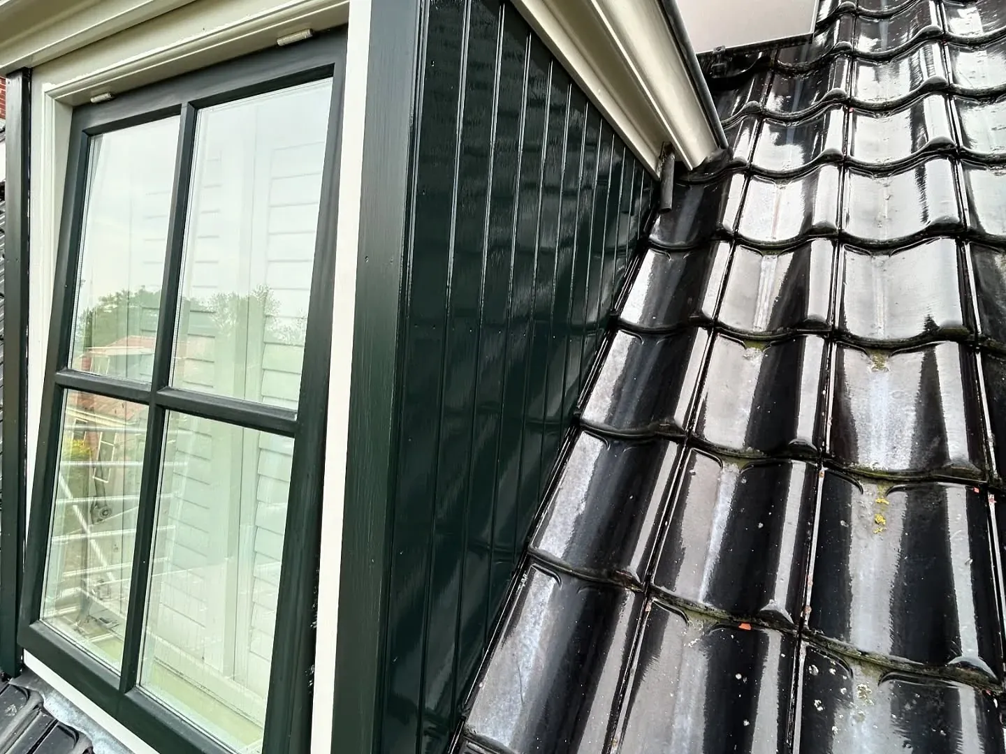 Detail van een groengeschilderde dakrand langs de pannen