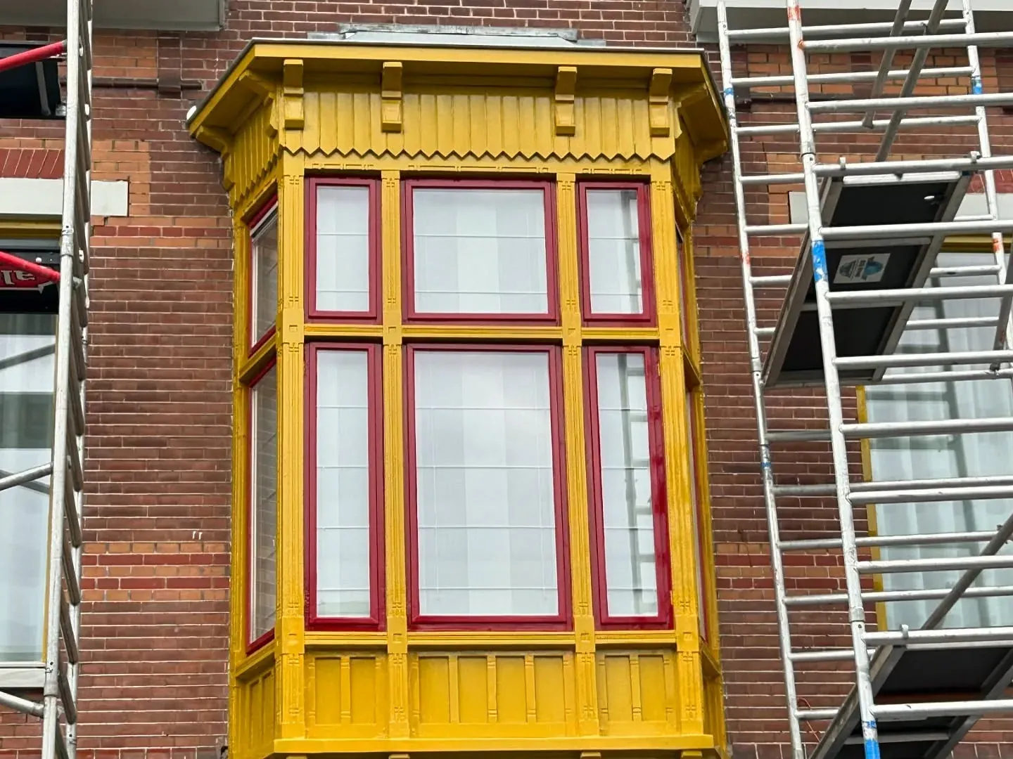 Erker met geel lijstwerk en rode roeden, met een ladder ernaast