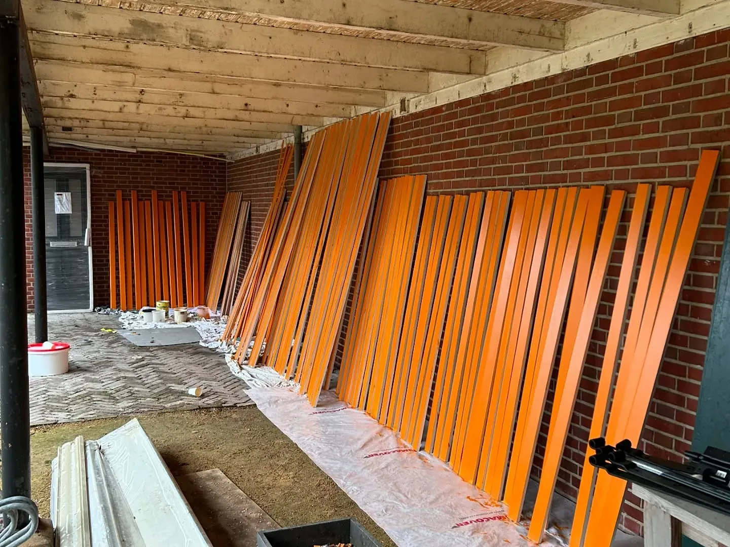 Rij oranje geschilderde latten, staand te drogen tegen een muur