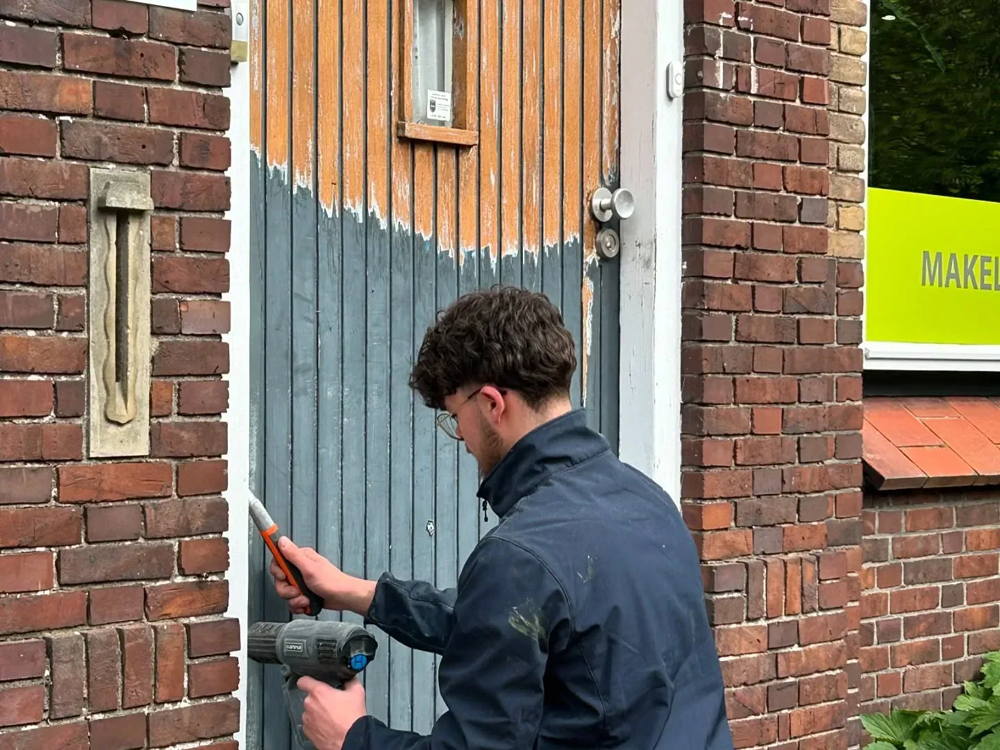 Schilder werkt met een kwast aan een houten geveldeel tussen twee bakstenen muren