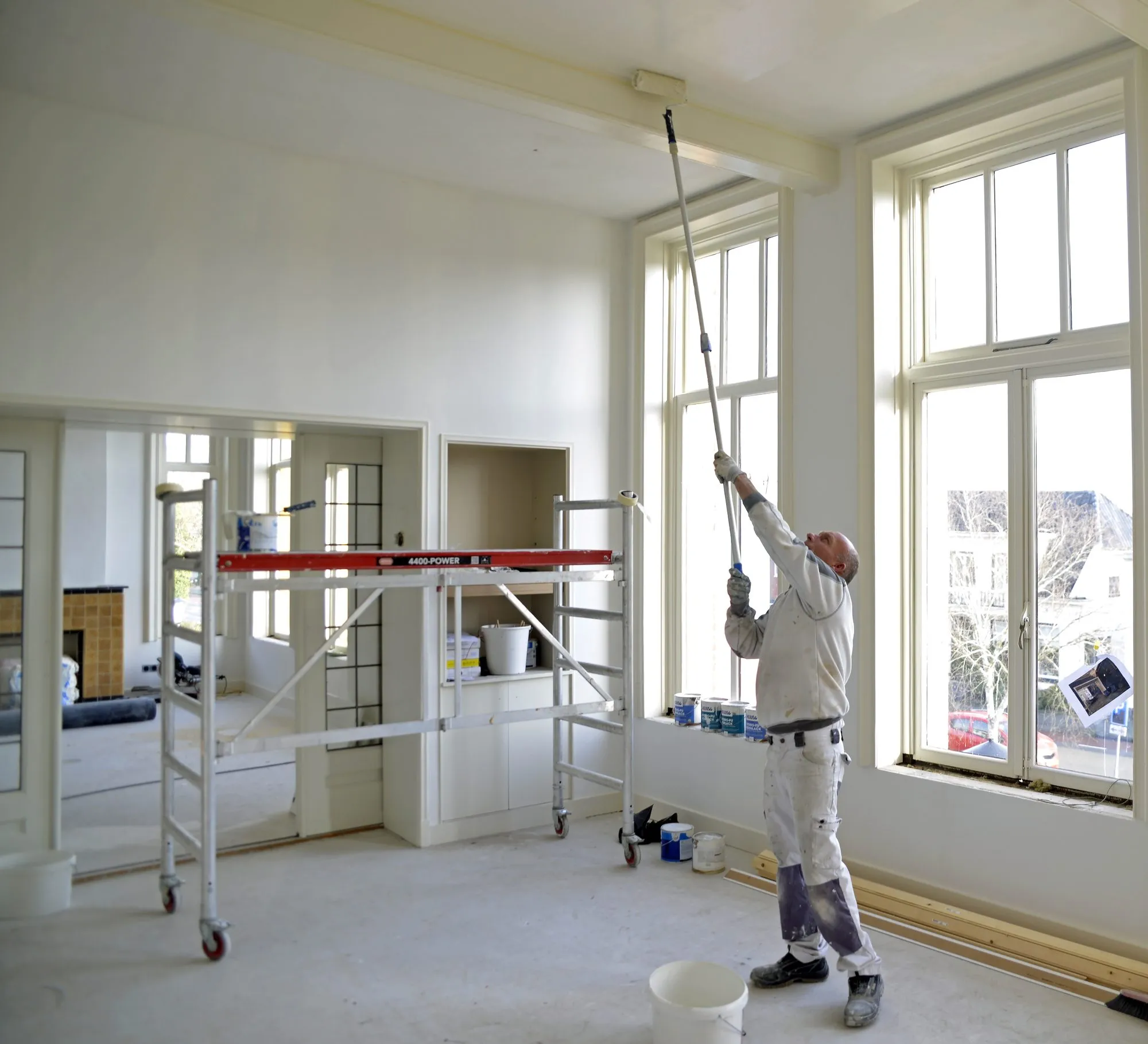 Schilder aan het werk in een lege kamer met hoge ramen