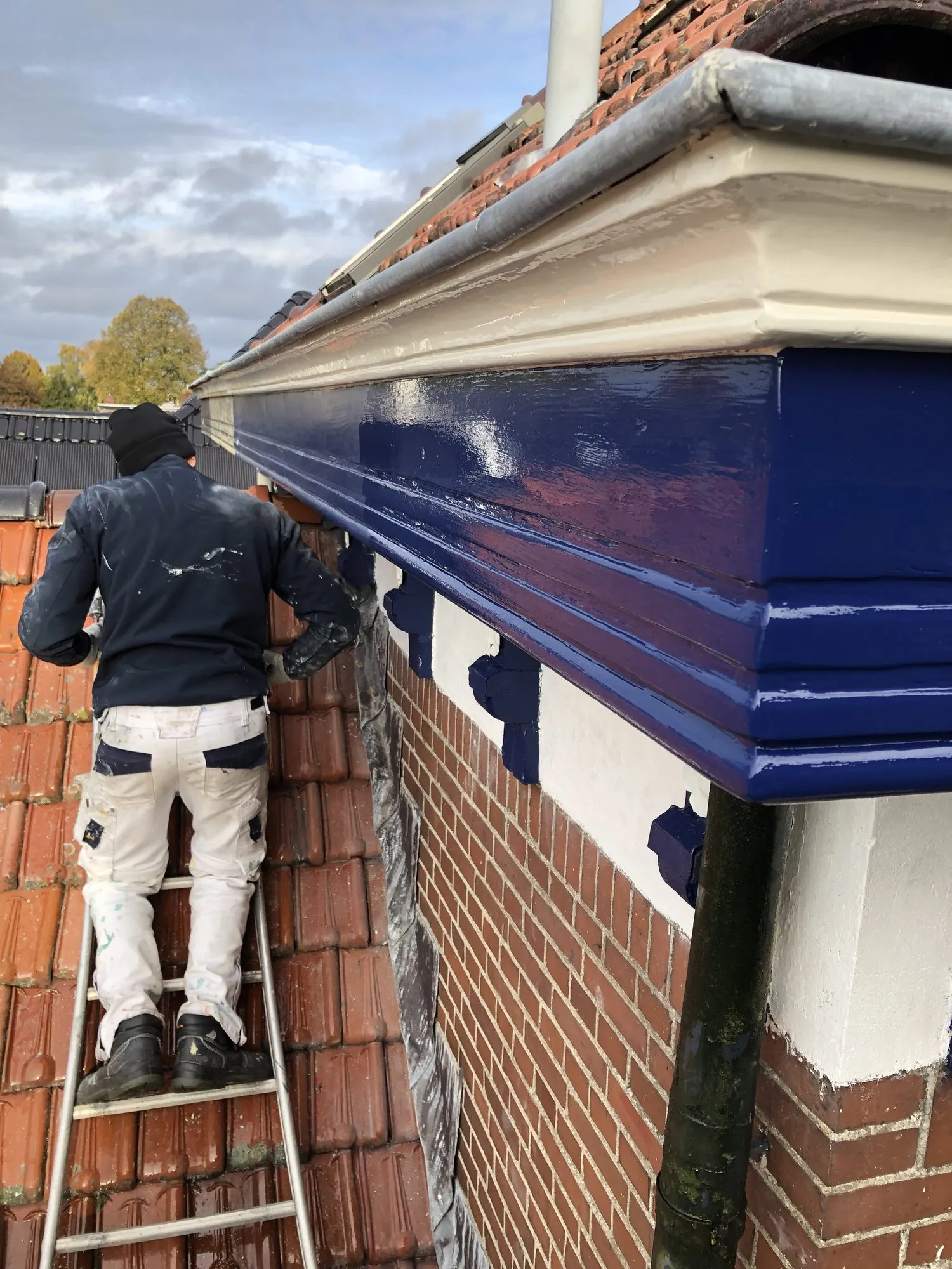 Schilder op een ladder die een dakgoot donkerblauw schildert