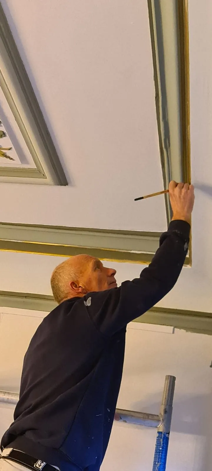Schilder die een plafondlijst met een kwast bijwerkt