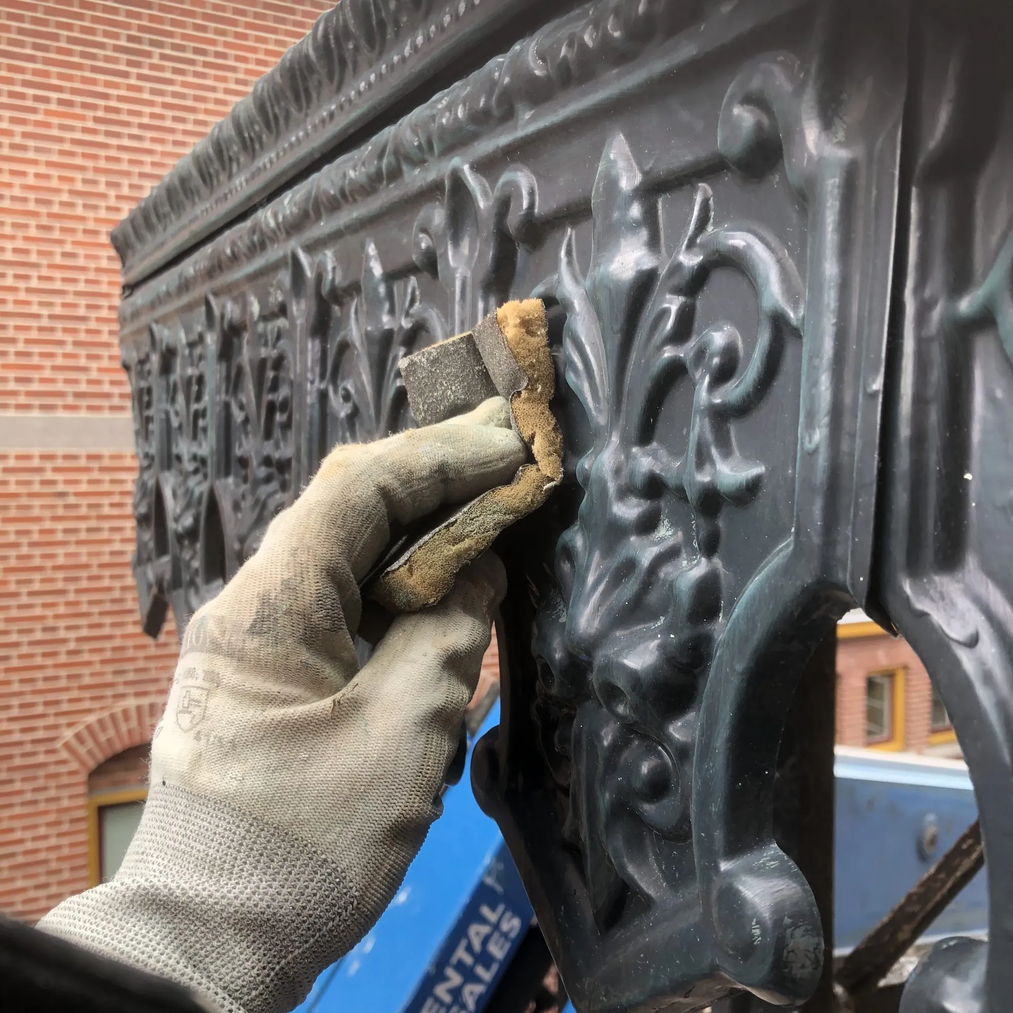 Hand met kwast die een gietijzeren ornament zwart schildert