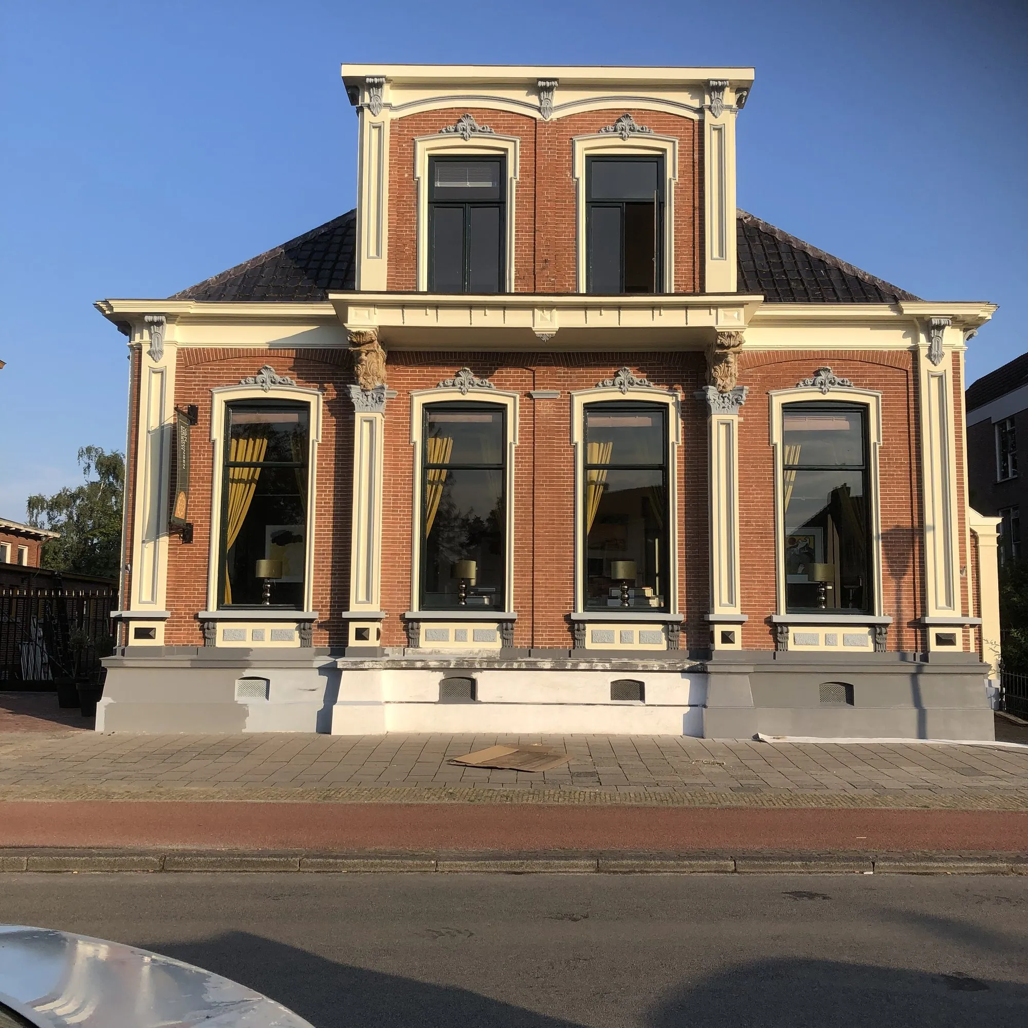 Voorgevel van een bakstenen herenhuis met crèmekleurige pilasters, ornamenten en een grijze plint