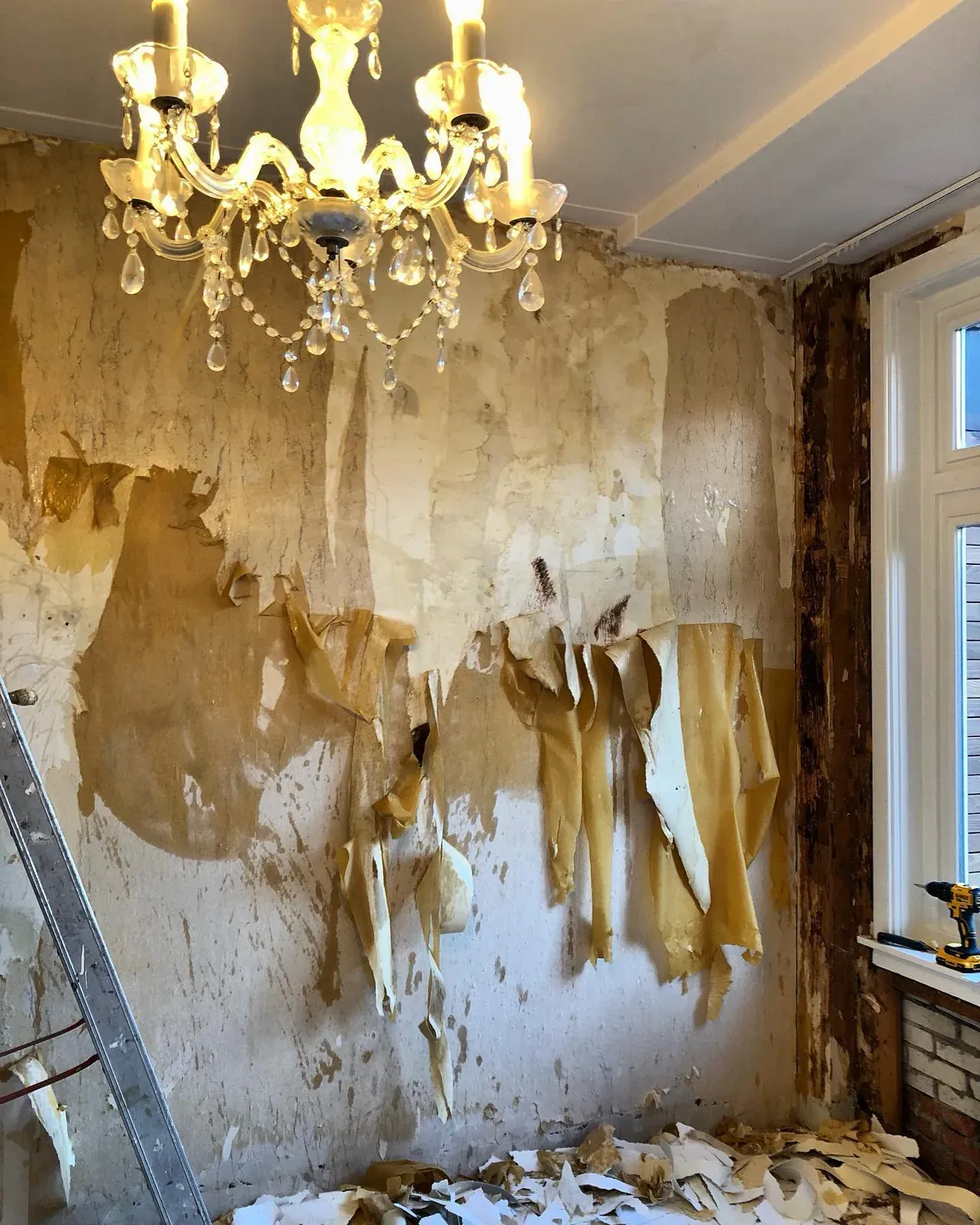 Kamer met kroonluchter waar het behang in stroken van de muur hangt