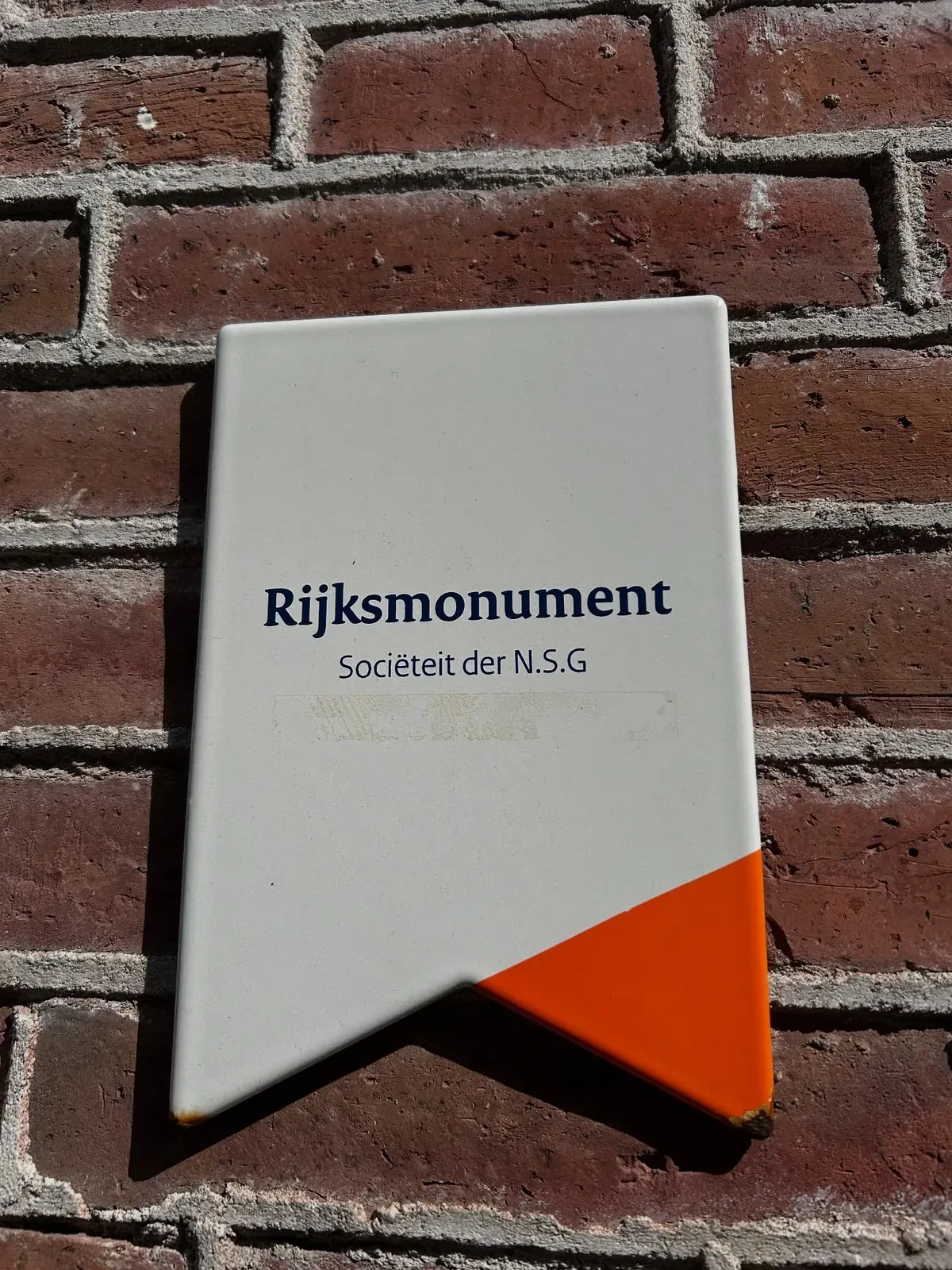 Wit bordje met het woord Rijksmonument tegen een bakstenen muur