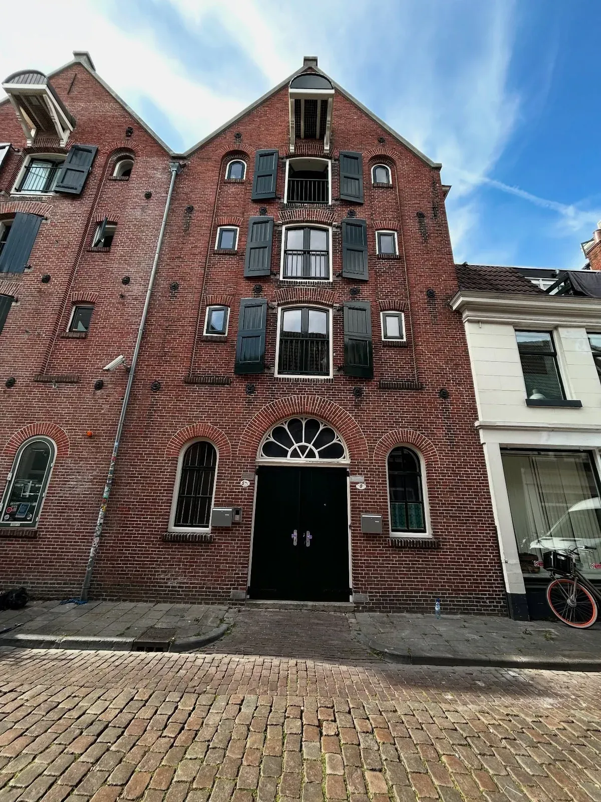 Bakstenen pakhuisgevel met luiken en een halfrond bovenlicht boven de deuren