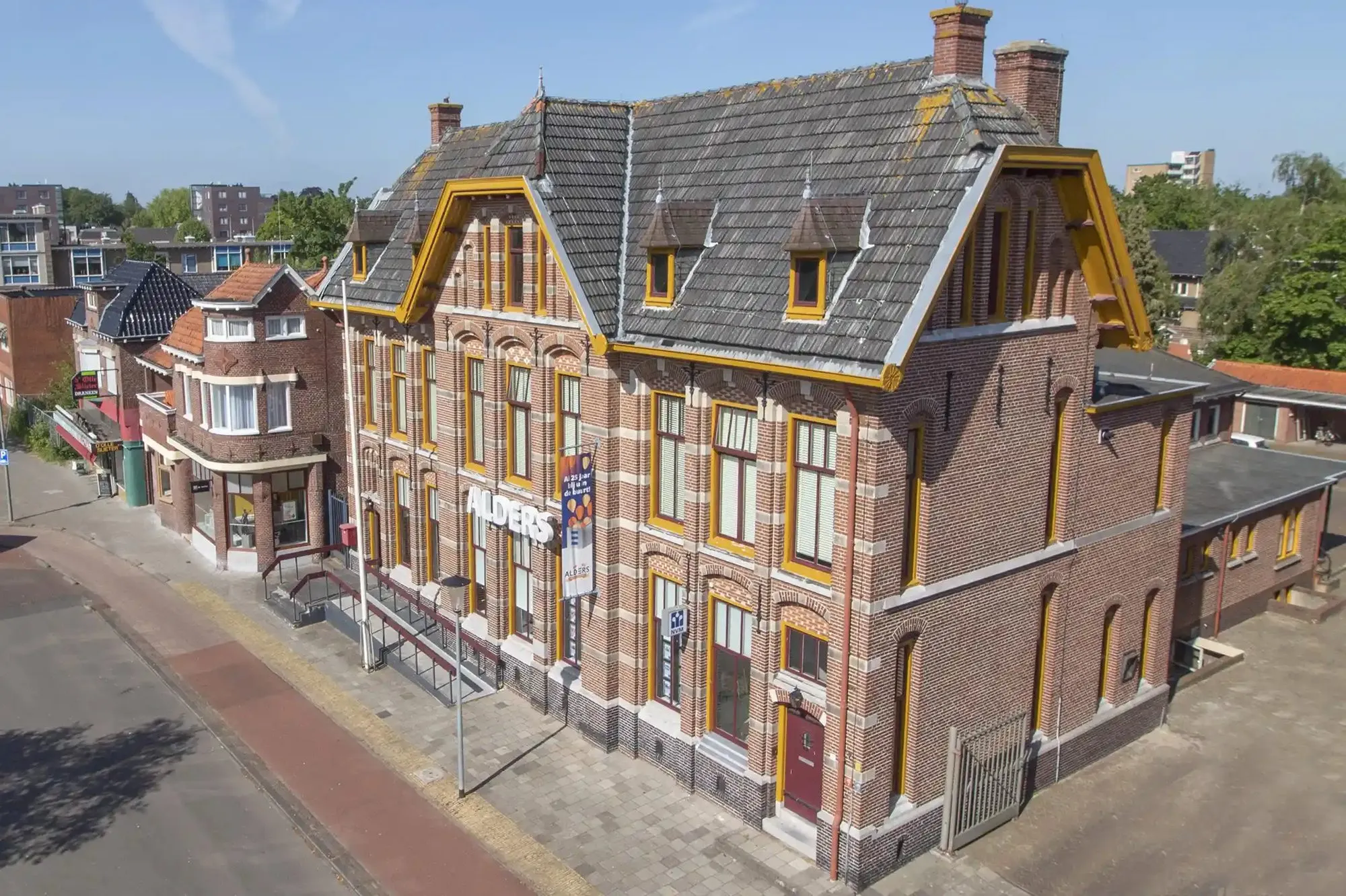 Luchtfoto van het voormalige postkantoor van Veendam, een bakstenen gebouw met okergele accenten en een leien dak
