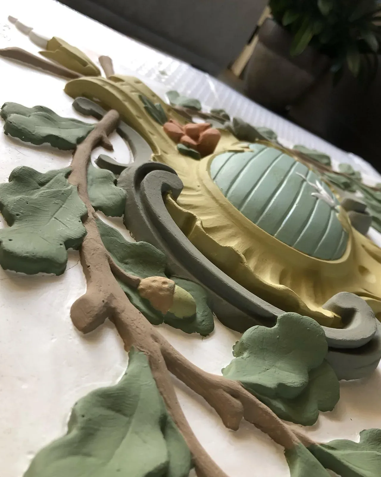 Close-up van een gipsornament met groene bladeren en een goudkleurig hart