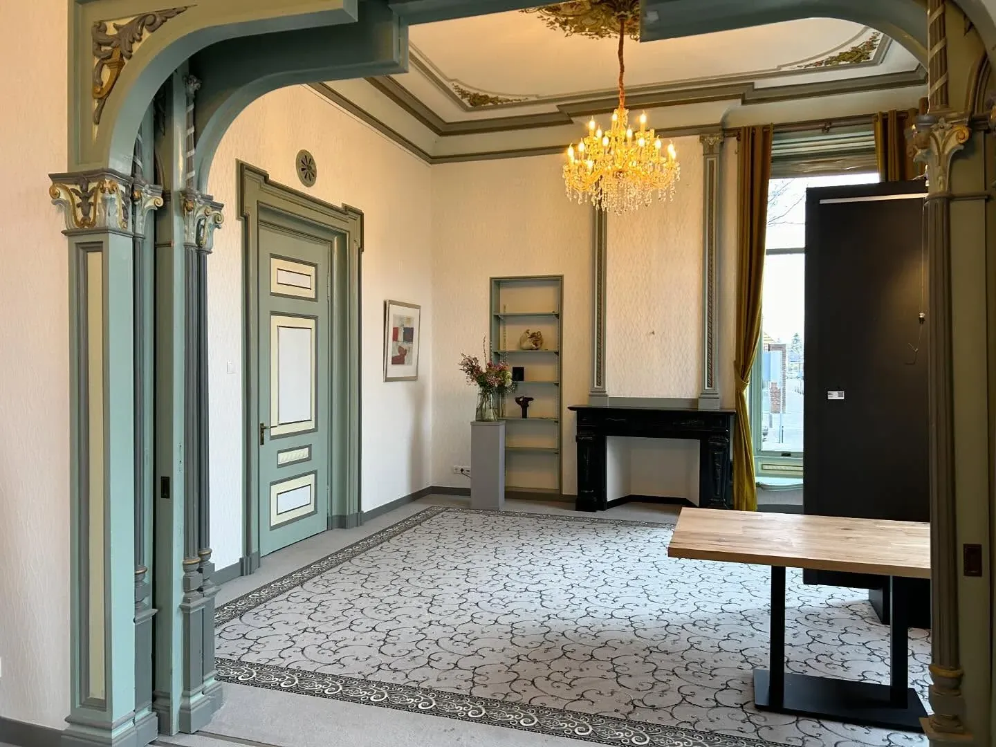 Salon met kroonluchter, groengeschilderde deuren en een geornamenteerd plafond