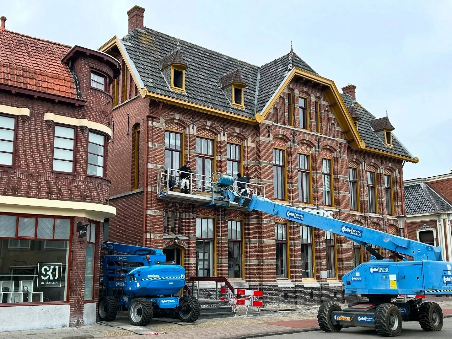 Pand met okergele kozijnen en een blauwe hoogwerker ervoor