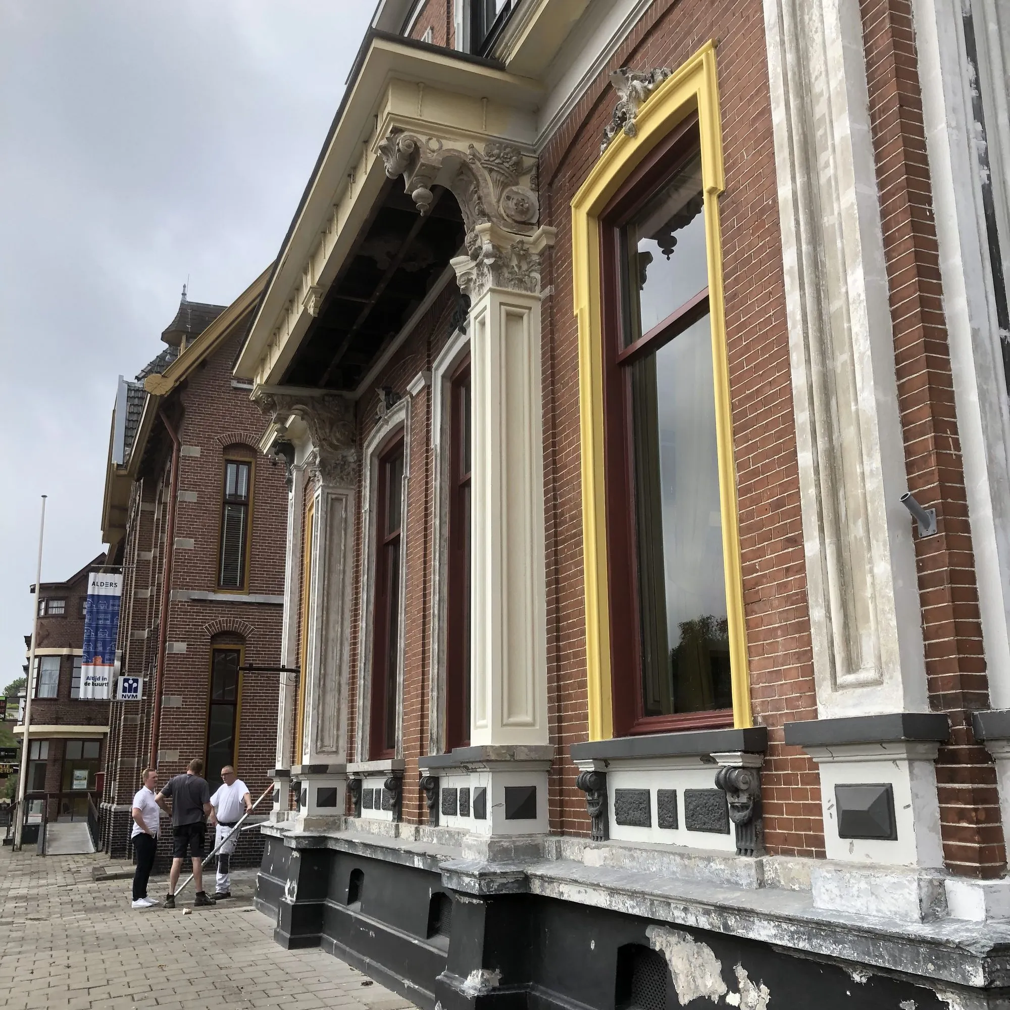 Zijgevel van een herenhuis uit 1888 met pilasters, kapitelen en okergele kozijnen, tijdens de restauratie