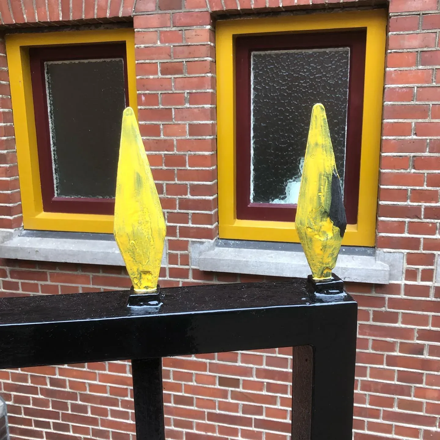 Vergulde speerpunten voor een bakstenen gevel met gele kozijnen