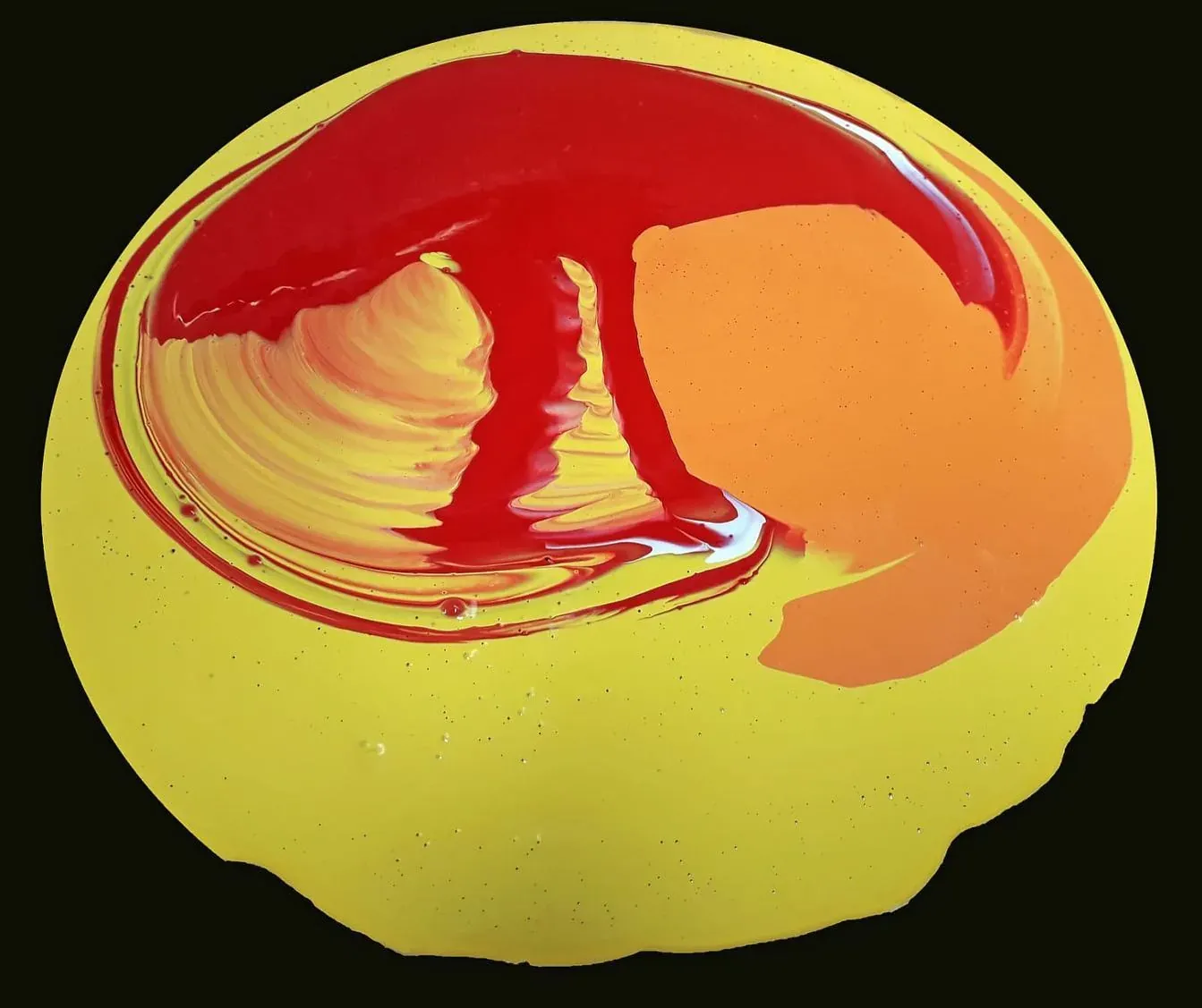 Verf in rood, oranje en geel die in elkaar draait op een ronde plaat